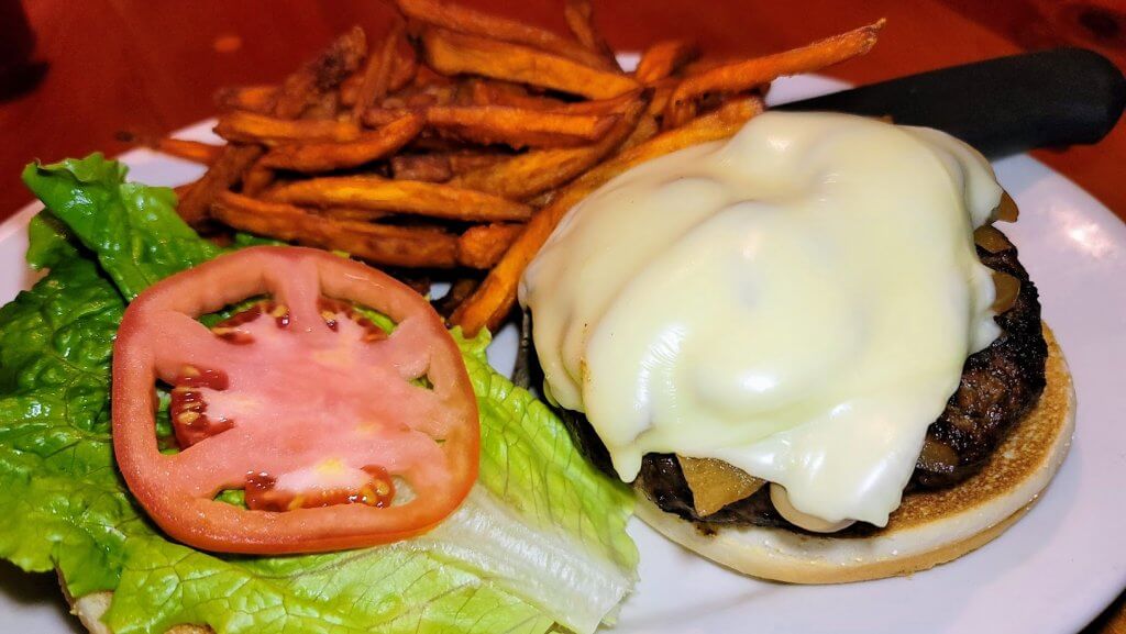 A burger opened up so you can see the melting cheese and fresh tomato. plated with a side of sweet potato fries.