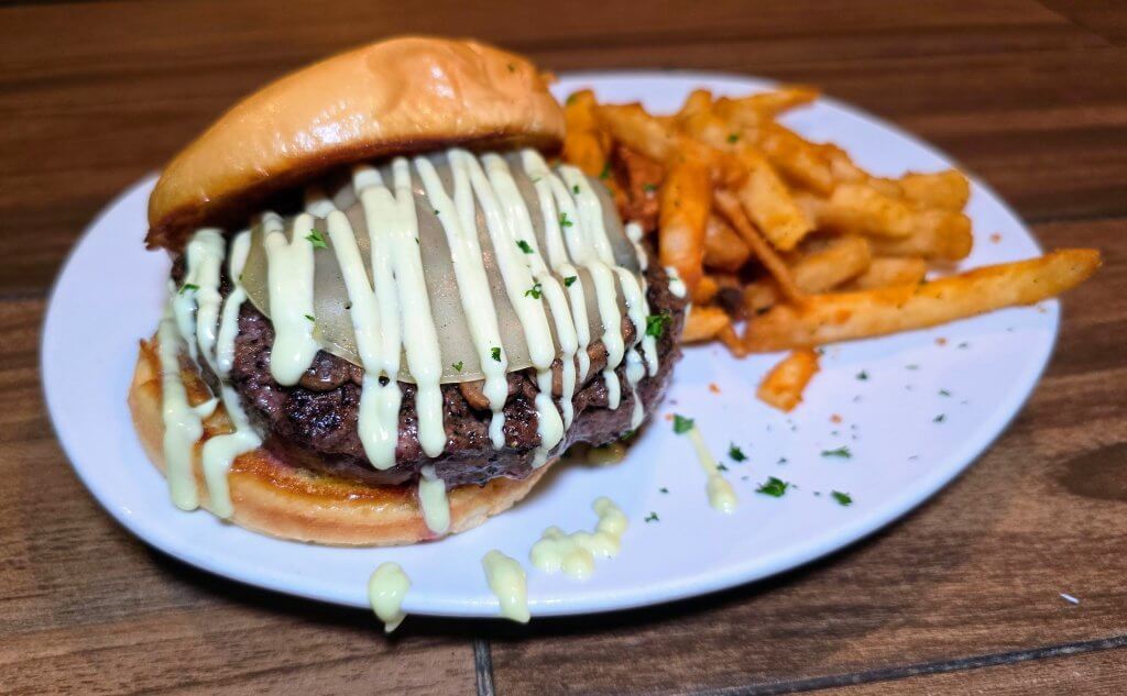 The Green Marlins Kung Fu Burger topped with sauteed mushrooms sweet sauce and provolone cheese. plated with fries.