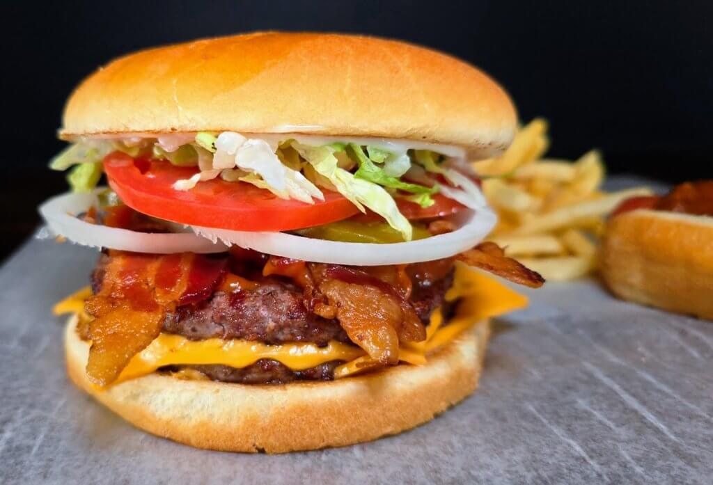 an up-close image of Quick Snaks OG Burger with bright red fresh tomato and thinly sliced onions and lettuce on top of two burger patty's and cheesy.