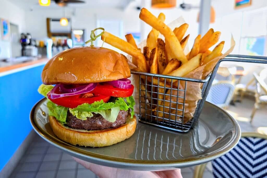 a thick burger patty on top of fresh burger buns topped with fresh red onion, lettuce, and tomato's. plated with a basket of fries.