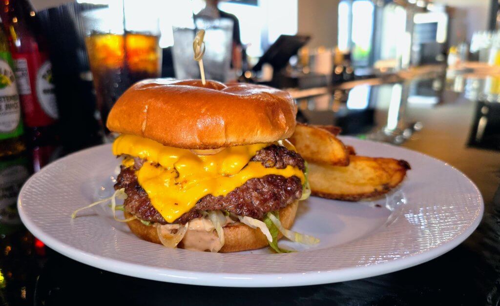 Touys downtown drive-in burger. a double stacked, smashed burger with melted american cheese and shredded lettuce, beefsteak tomato and a brioche bun. served with potato wedges.