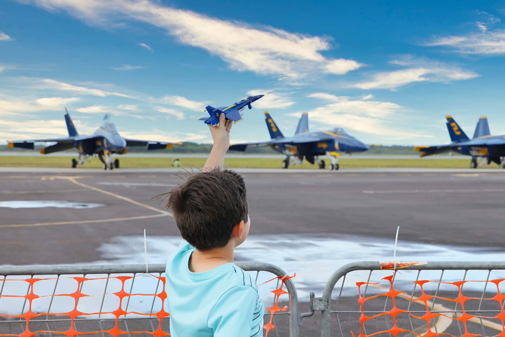 A little Boy holding up a toy plane at the Vero Beach Air Show with the Blue angels planes in the background.