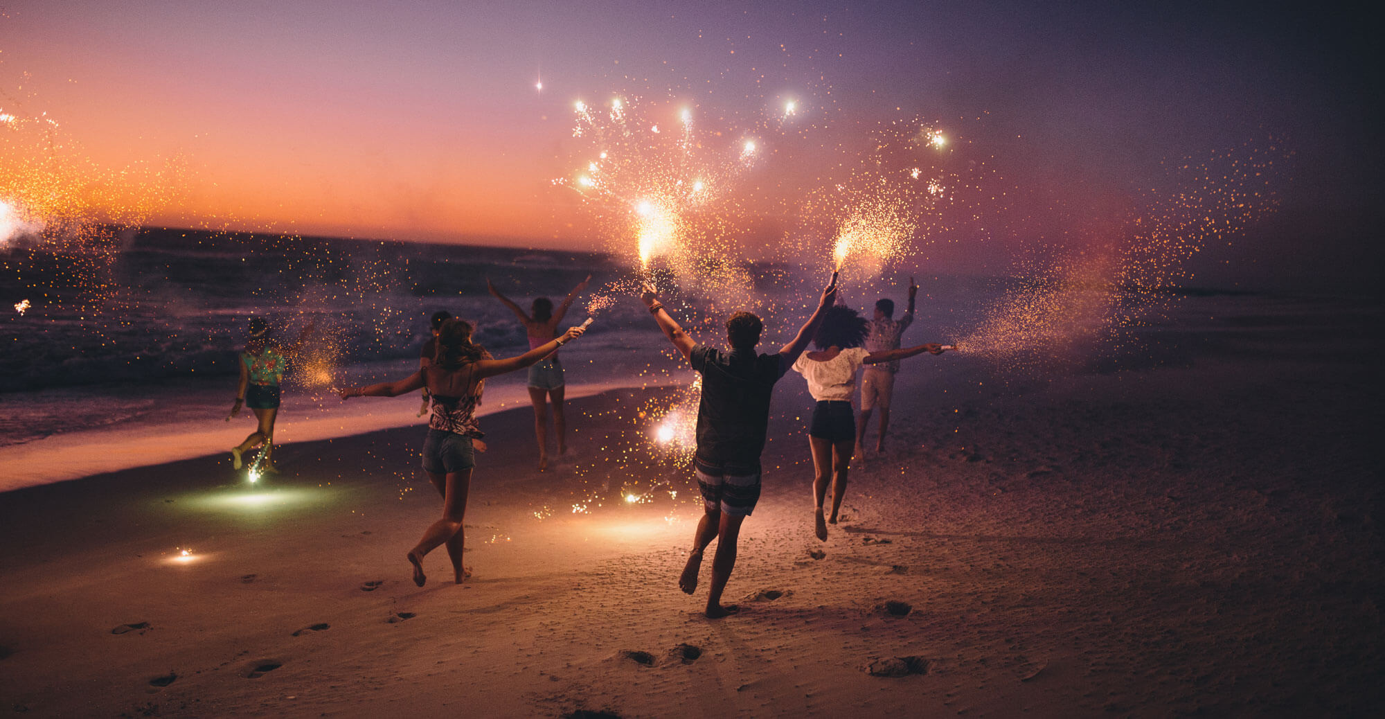 Friends running with fireworks on a beach after sunset