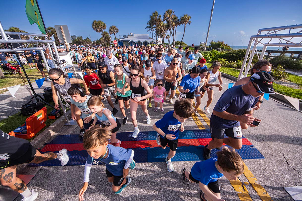 People running through the start line at the tipsy turtle two mile race with coastal connections.